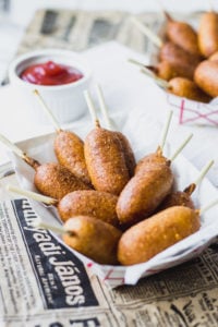 Mini Carrot Corn Dogs in serving container with ketchup on newspaper