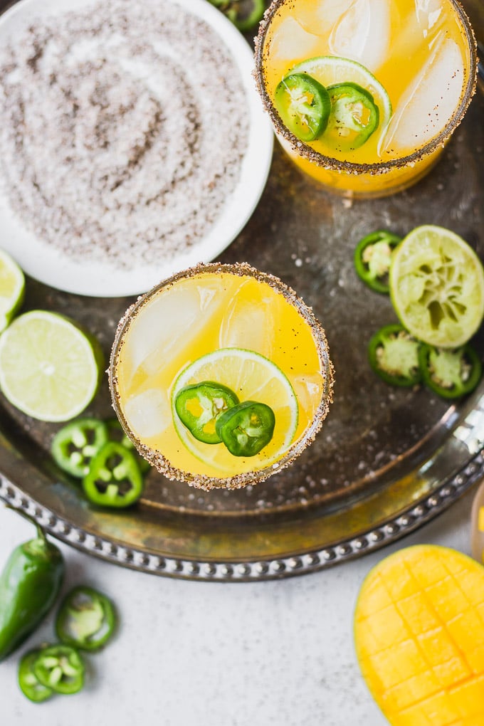 Mango margaritas on tray with jalapenos, lime, and mangos.