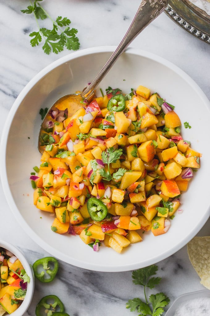 White bowl of peach salsa with spoon.
