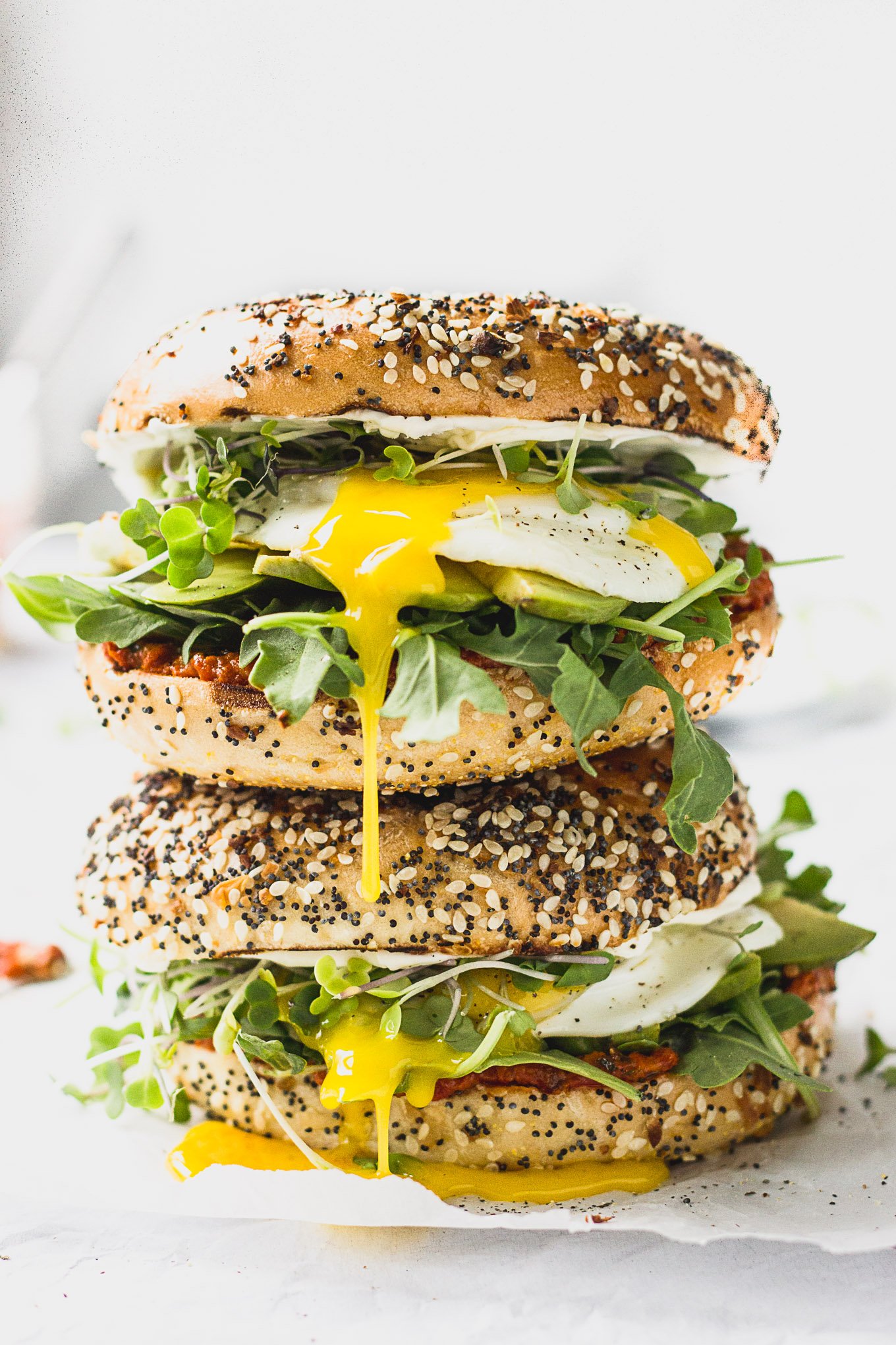 Two bagel sandwiches stacked on each other with dripping yolk.