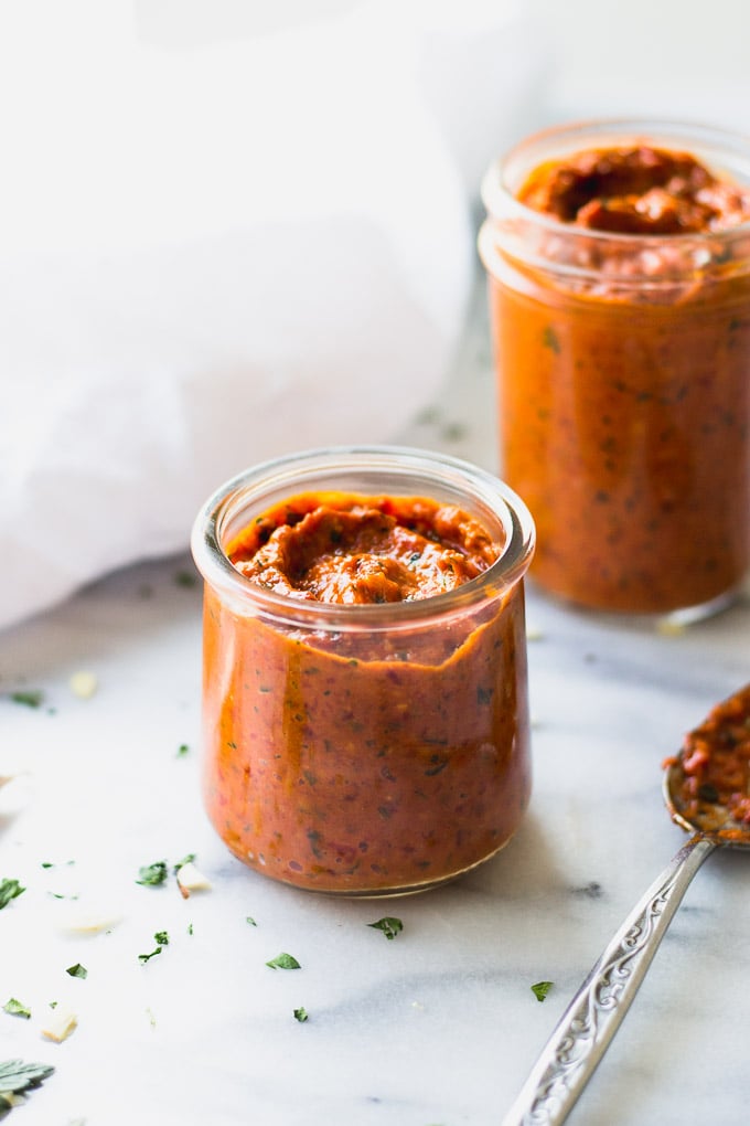 Two jars of romesco sauce with a spoon next to them.