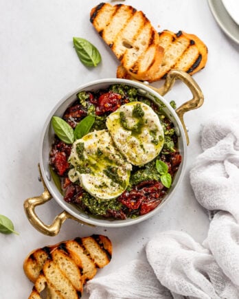 Serving dish with tomato jam, pesto, and burrata next to baguette slices.