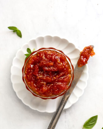 Tomato jam in glass bowl next to knife.