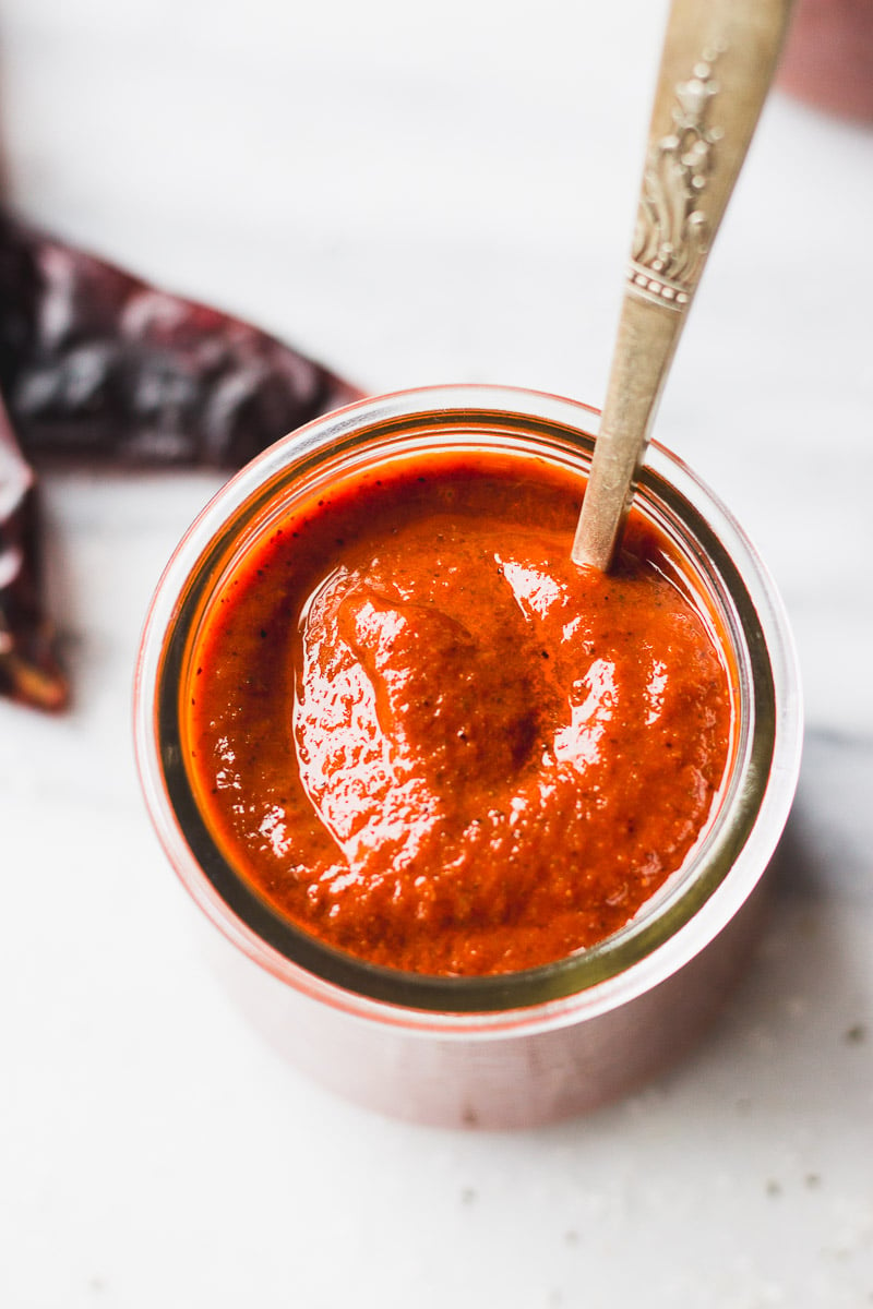 red enchilada sauce in a jar with a spoon