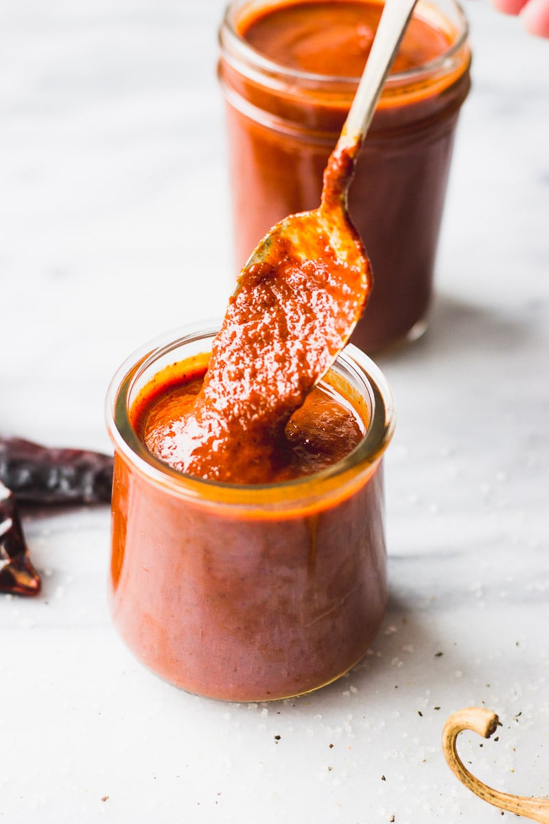 red enchilada sauce in jar with spoon scooping