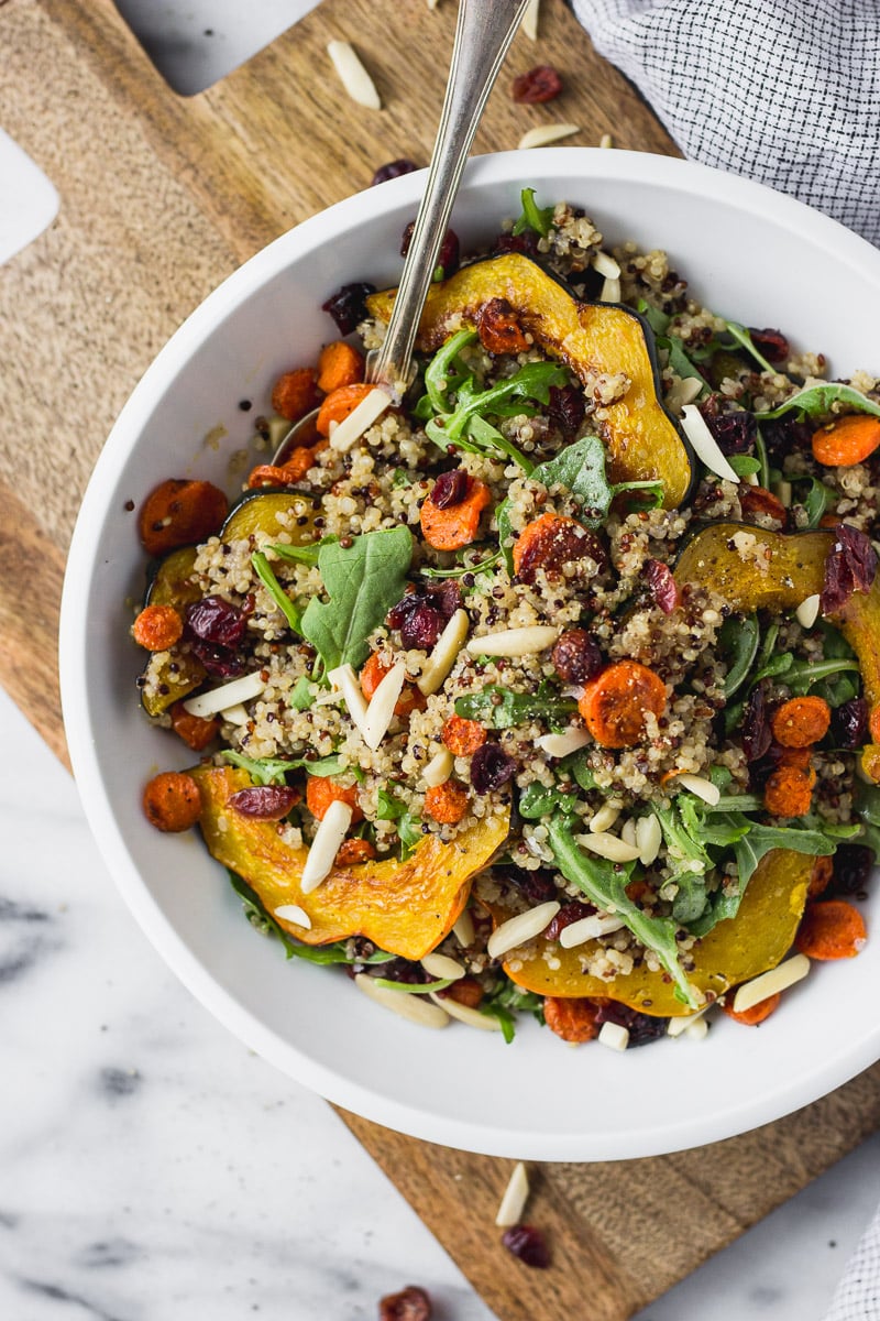 fall acorn squash salad with carrots and arugula in white bowl with spoon by fork in the kitchen