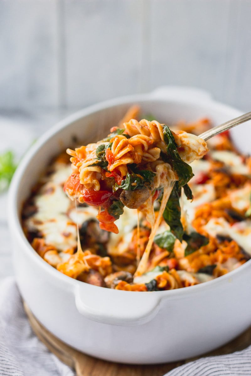 vegetable baked pasta in white casserole dish with scoop being lifted