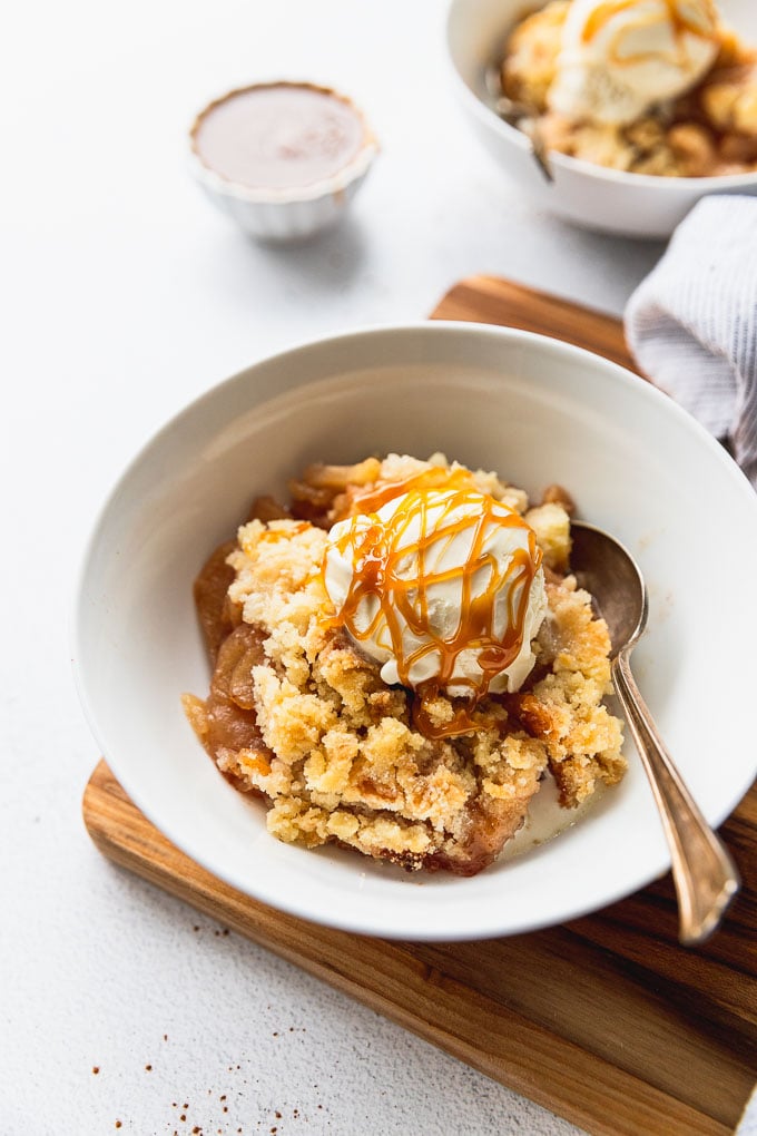 Apple crisp without oats topped with ice cream and caramel drizzle in bowl.