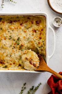 Casserole dish with scalloped potatoes and a spoon taking a scoop.