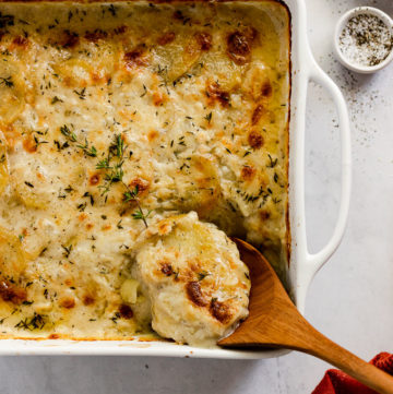Casserole dish with scalloped potatoes and a spoon taking a scoop.