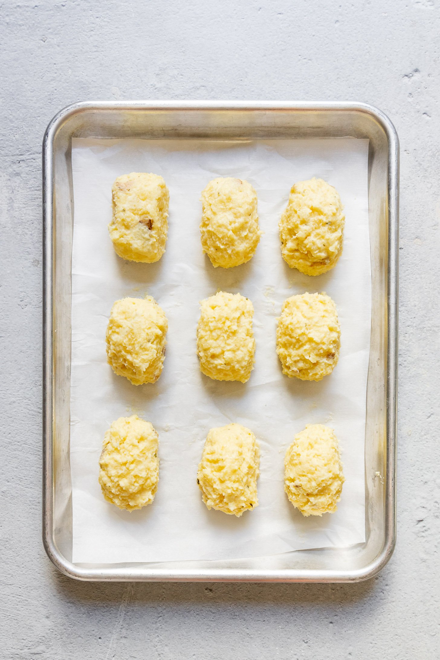 Potato croquettes shaped on baking sheet.