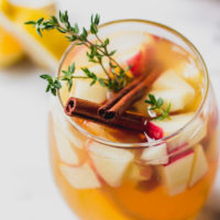 apple cider sangria in glass with cinnamon, thyme, and apples by fork in the kitchen