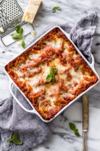 Vegetarian Spinach Ricotta Lasagna in white casserole dish with linen and knife by Fork in the Kitchen