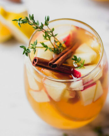 apple cider sangria in glass with cinnamon, thyme, and apples by fork in the kitchen
