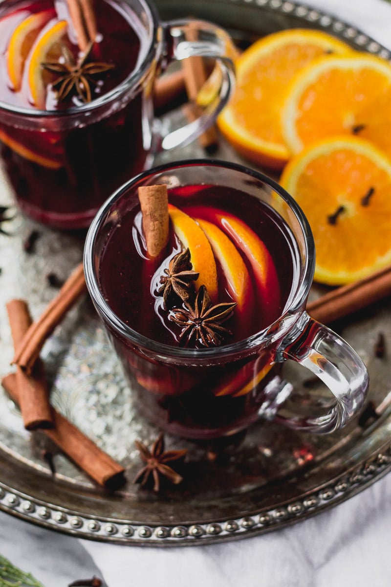 Glass mug with mulled red wine, cinnamon, and orange slices on tray.