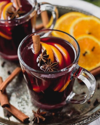 glass mug with mulled red wine, cinnamon, and orange slices on tray by fork in the kitchen