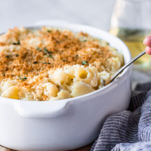 white wine mac and cheese being scooped out of casserole dish by fork in the kitchen