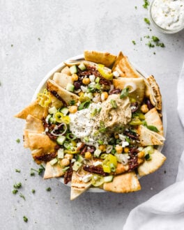 Bowl of Mediterranean nachos with pita, toppings, and tzatziki sauce in a jar.