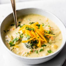 broccoli cauliflower cheddar soup in bowls with baguette by fork in the kitchen
