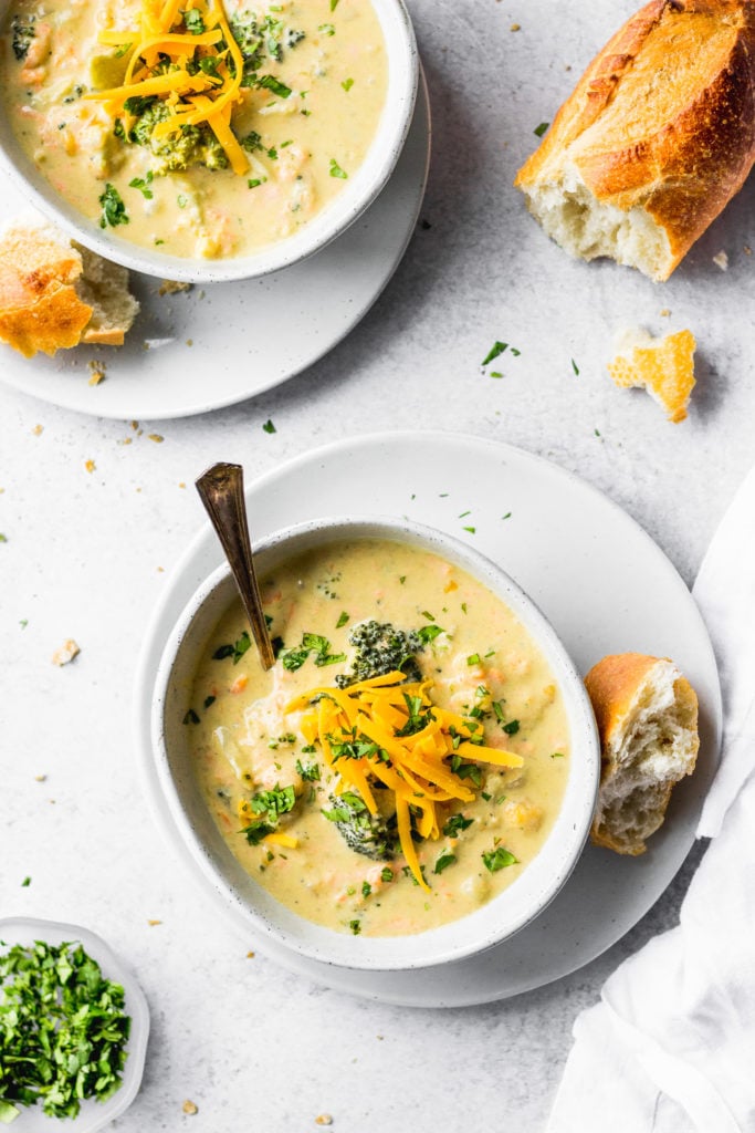 Broccoli cauliflower cheddar soup in bowls with baguette pieces next to bowl of parsley.