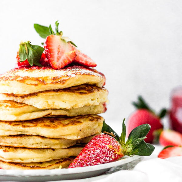 lemon mascarpone pancakes with strawberry sauce stacked on plate by fork in the kitchen