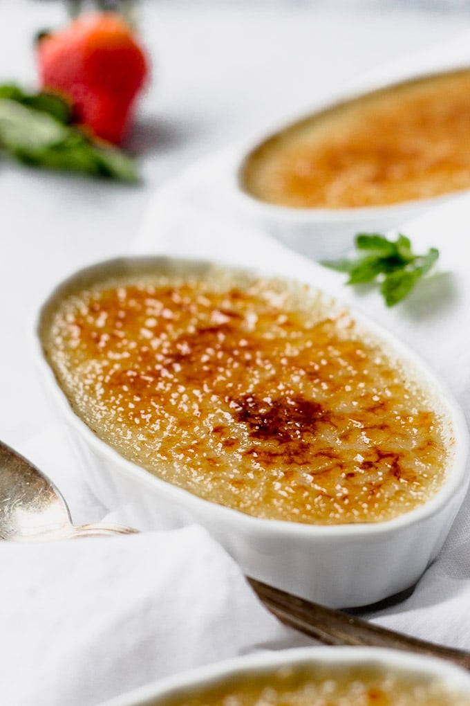 vanilla bean creme brulee in white ramekin with berries and spoon by fork in the kitchen