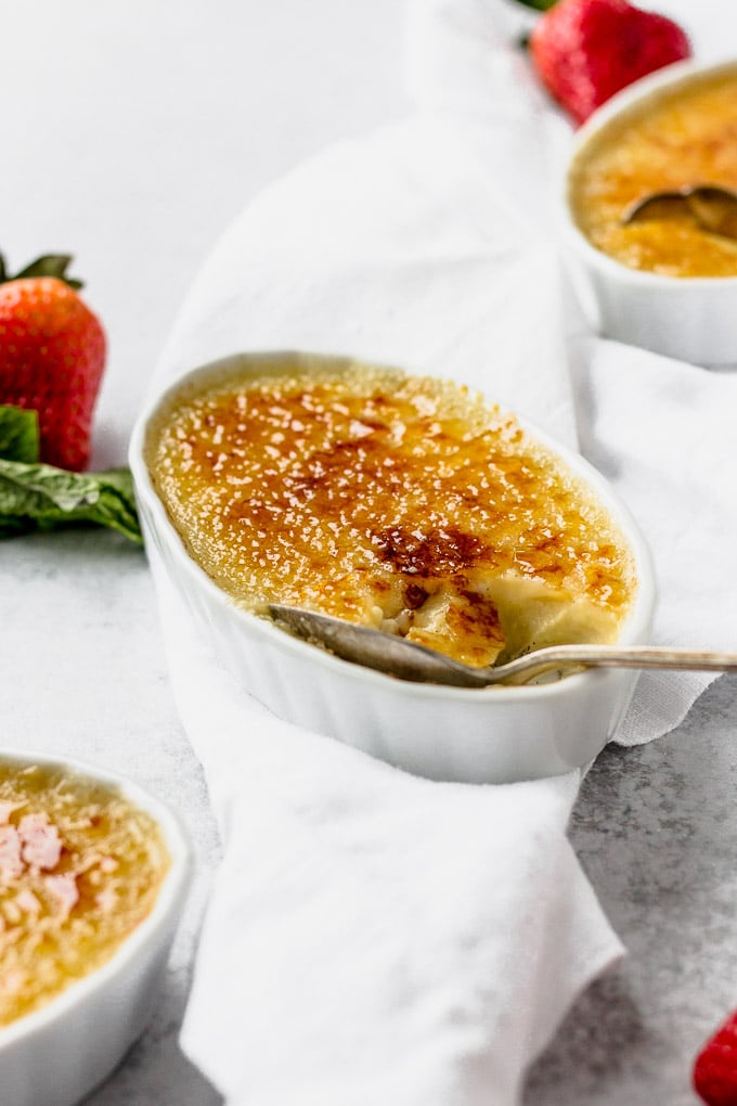 vanilla bean creme brulee in white ramekin with berries and spoon by fork in the kitchen