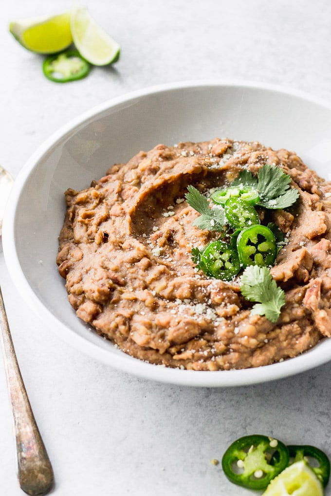 vegetarian refried beans in white bowl with jalapenos and cilantro by fork in the kitchen