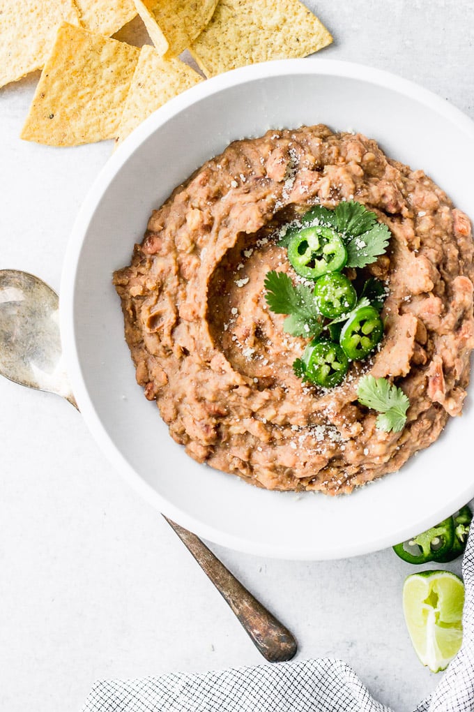 vegetarian refried beans in white bowl with jalapenos and cilantro by fork in the kitchen
