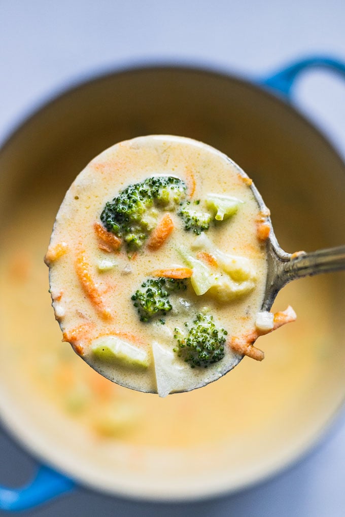 Scoop of broccoli cauliflower cheese soup over dutch oven.