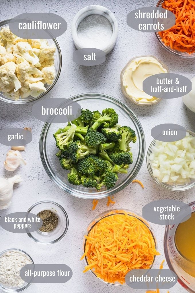 Bowl of ingredients: cauliflower and broccoli florets, salt, shredded carrots, butter, half and half, onion, vegetable stock, shredded cheese, flour, spices, and garlic.