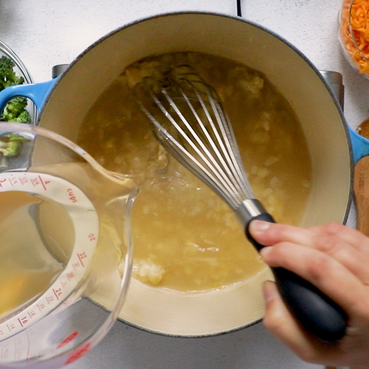 Whisking in vegetable stock into pot.