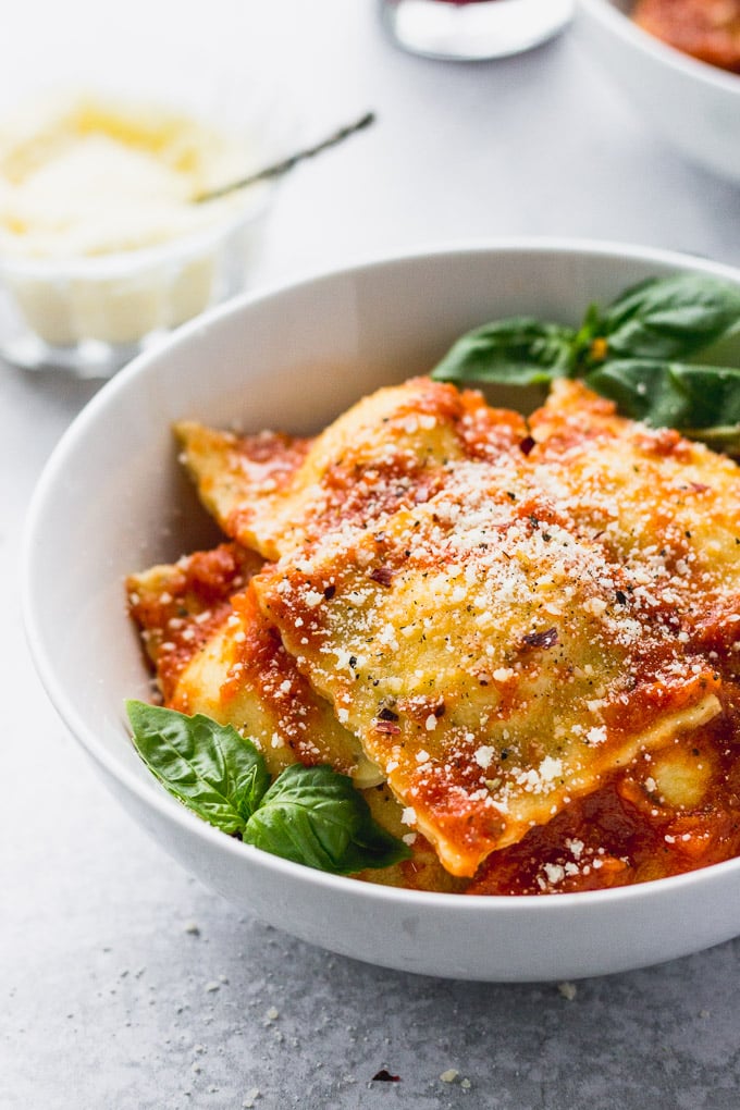White bowl with ravioli and basil leaves.