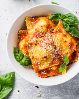 Bowl of cheese ravioli with basil leaves inside and around.