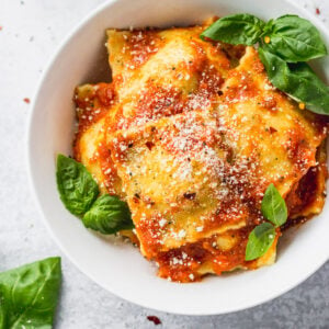 Bowl of cheese ravioli with basil leaves inside and around.