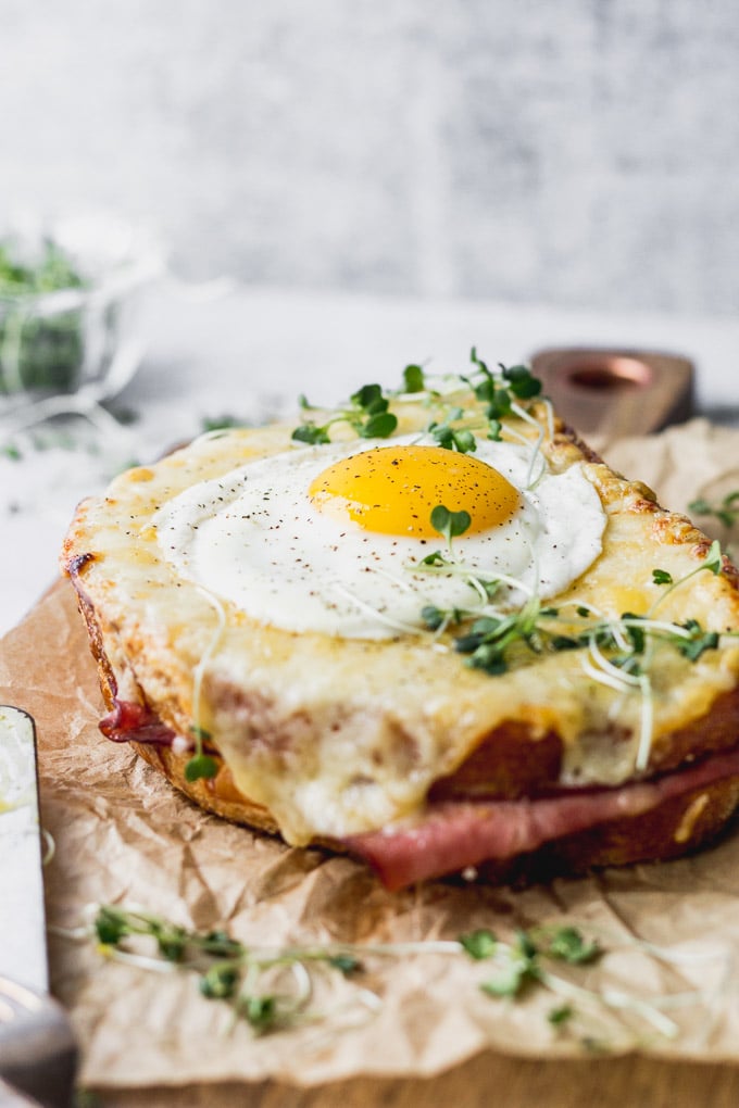 Fried egg on top of croque madame sandwich on a cutting board.