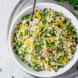 tuna orzo pasta salad in white bowl with spoon by fork in the kitchen