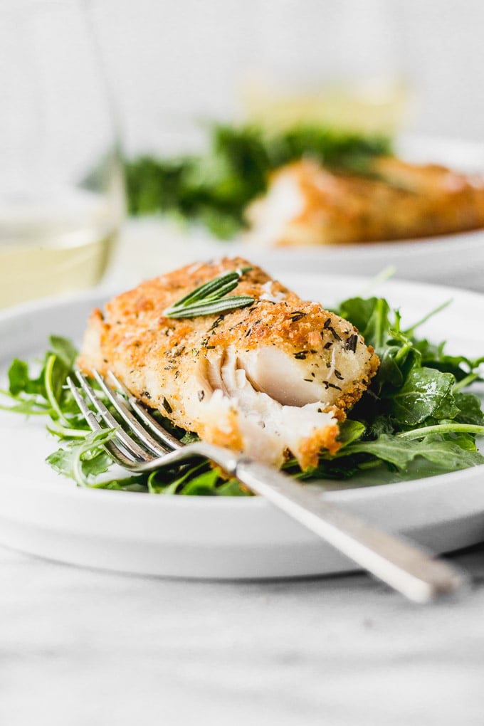 Fish flaked open on bed of arugula next to a fork on a white plate.