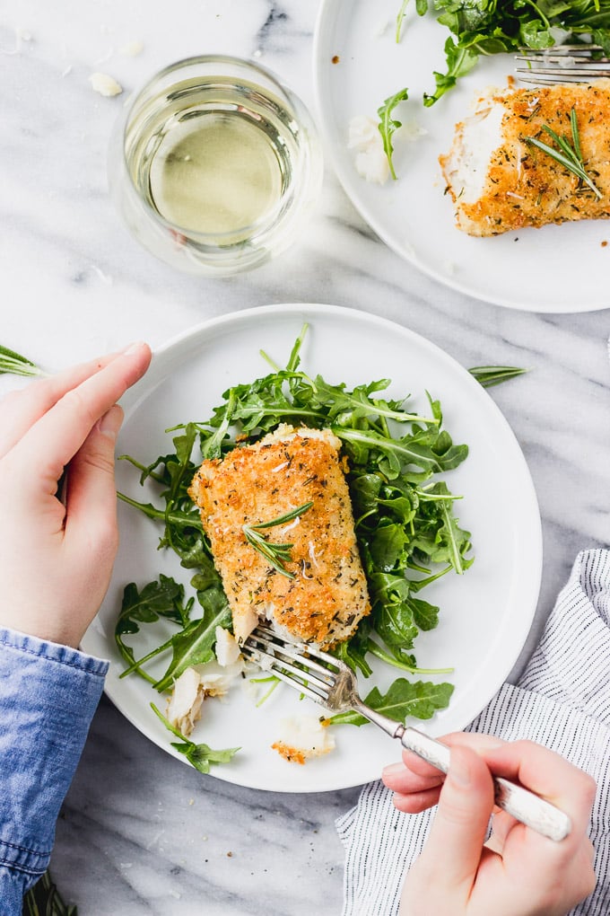 Hands holding plate and fork with arugula and fish.