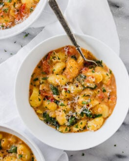 White bowl of vegetarian gnocchi with spinach and tomatoes.