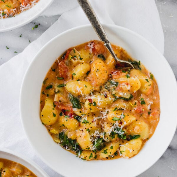 White bowl of vegetarian gnocchi with spinach and tomatoes.