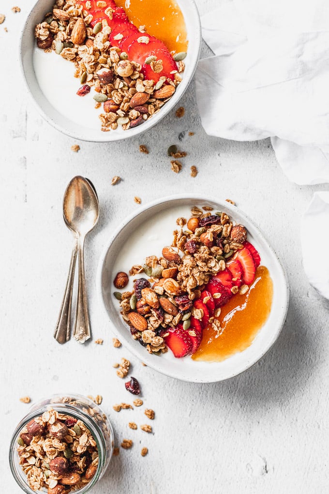 two bowls with homemade cinnamon crunch granola with strawberries and apricot jam