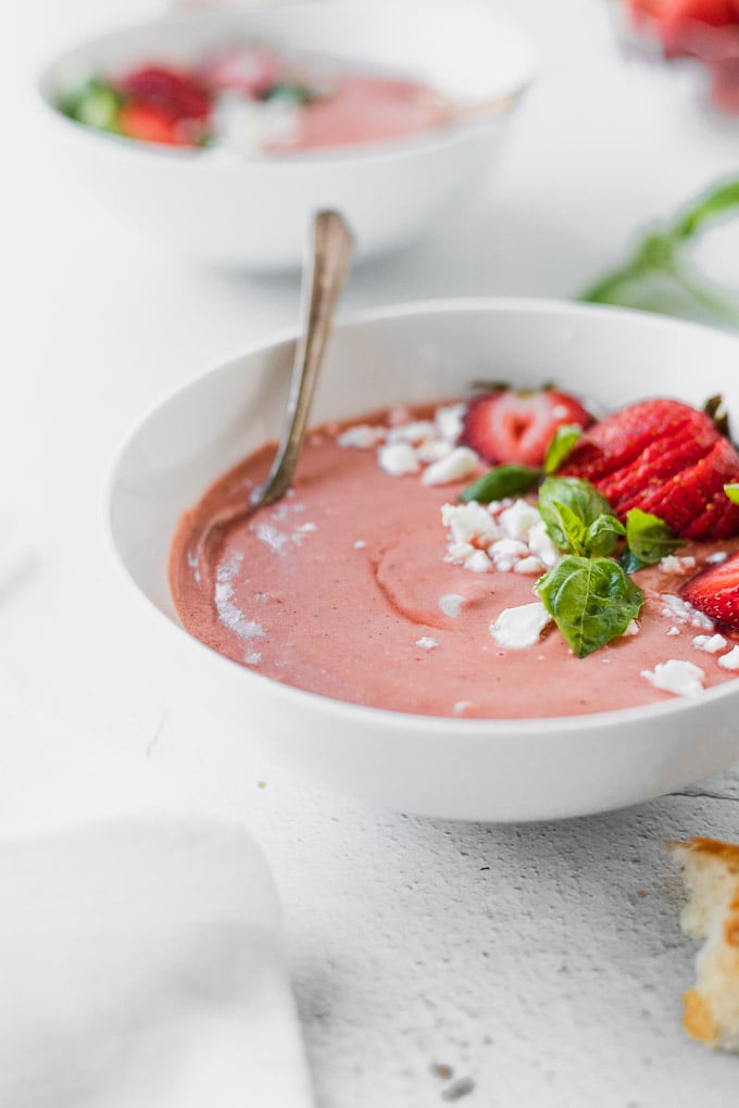 white bowl with pink strawberry basil gazpacho with spoon