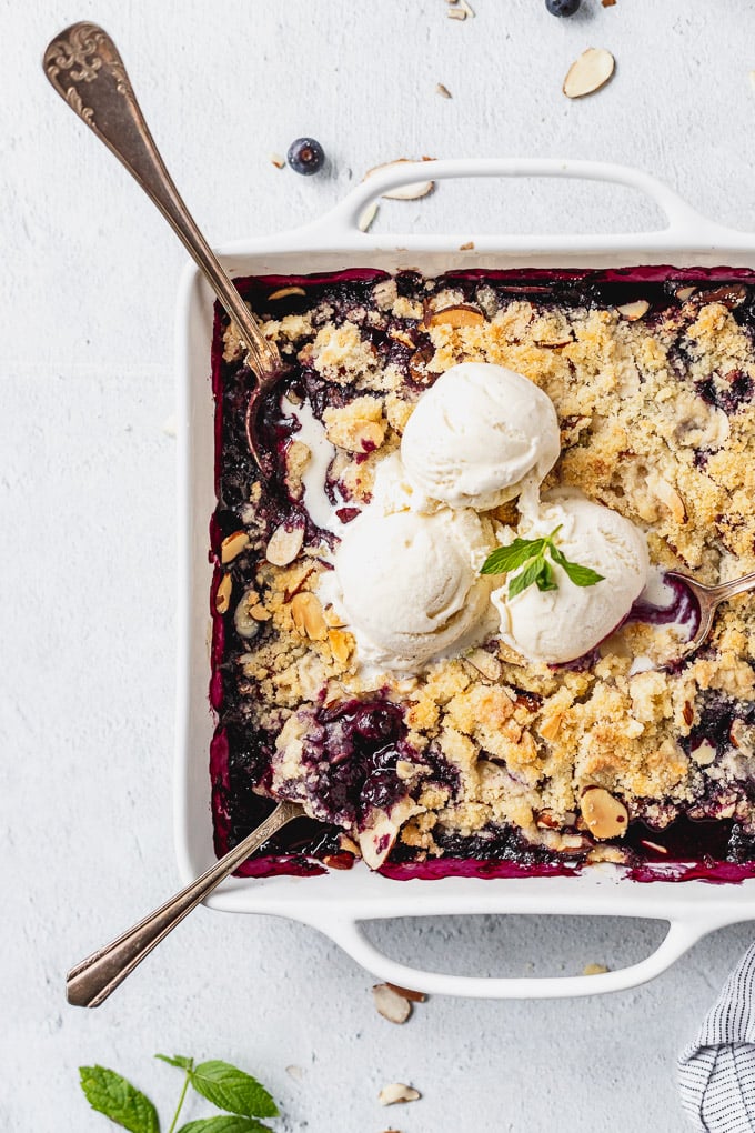 blueberry almond crisp with vanilla ice cream in a white baker and spoons