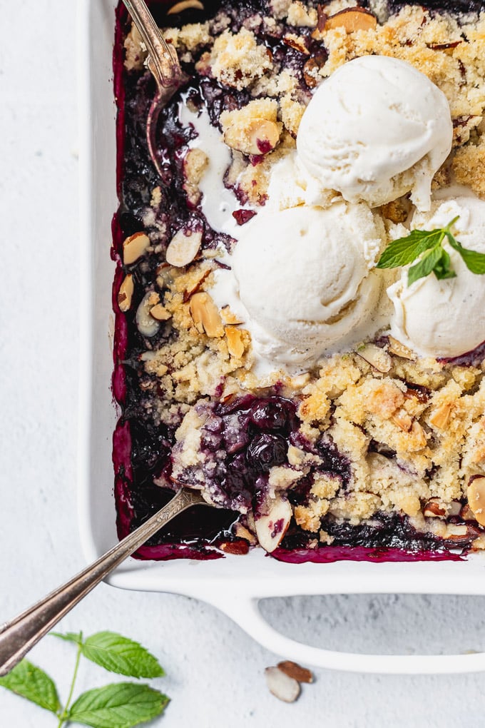 blueberry almond crisp with vanilla ice cream in a white baker and spoons