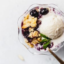 blueberry almond crisp with vanilla ice cream in glass bowl