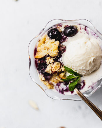 blueberry almond crisp with vanilla ice cream in glass bowl