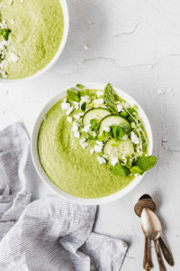 green cucumber soup in white bowls with linen next to them