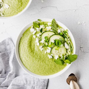green cucumber soup in white bowls with linen next to them