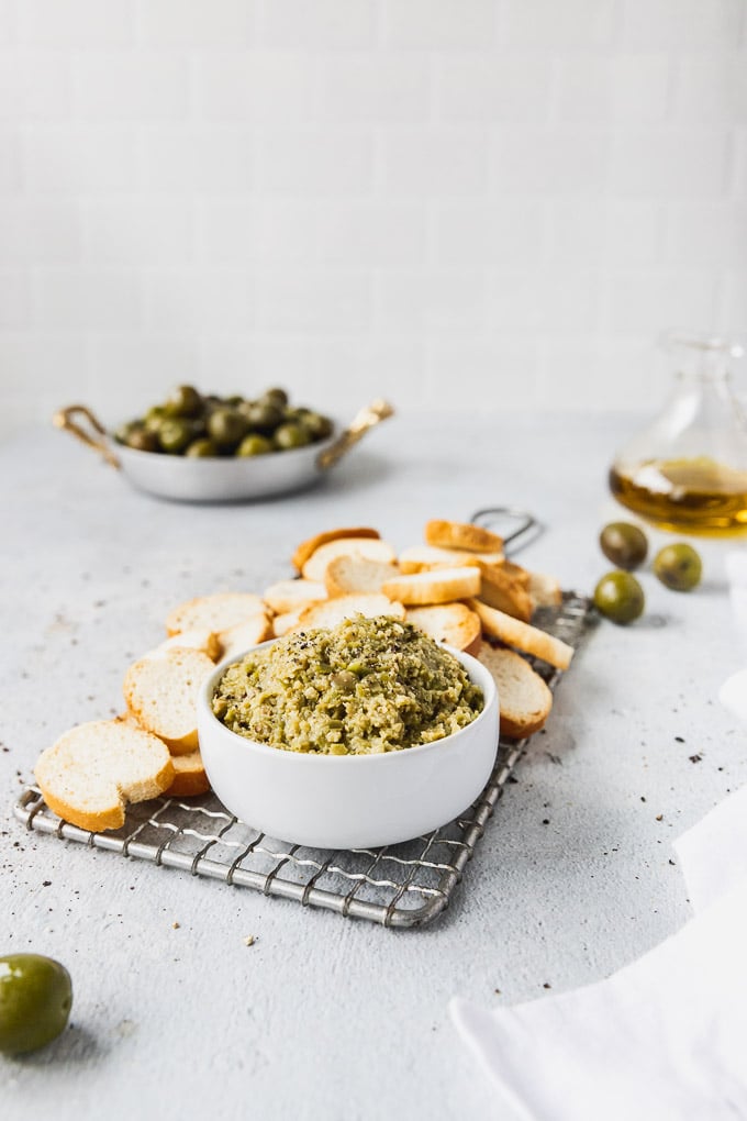 Green olive tapenade with baguette crisps side view.